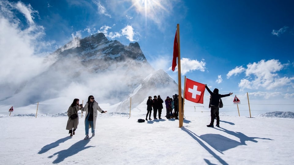 Touristen im Schnee mit Schweizer Fahne und Bergen.