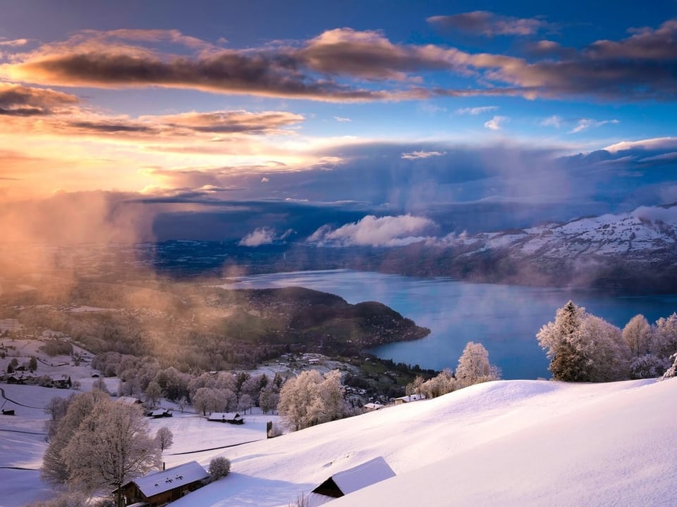 Winterlandschaft mit schneebedeckten Hügeln und einem See bei Sonnenuntergang