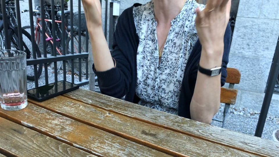 Eine junge Frau sitzt am Tisch und artikuliert mit den Händen.