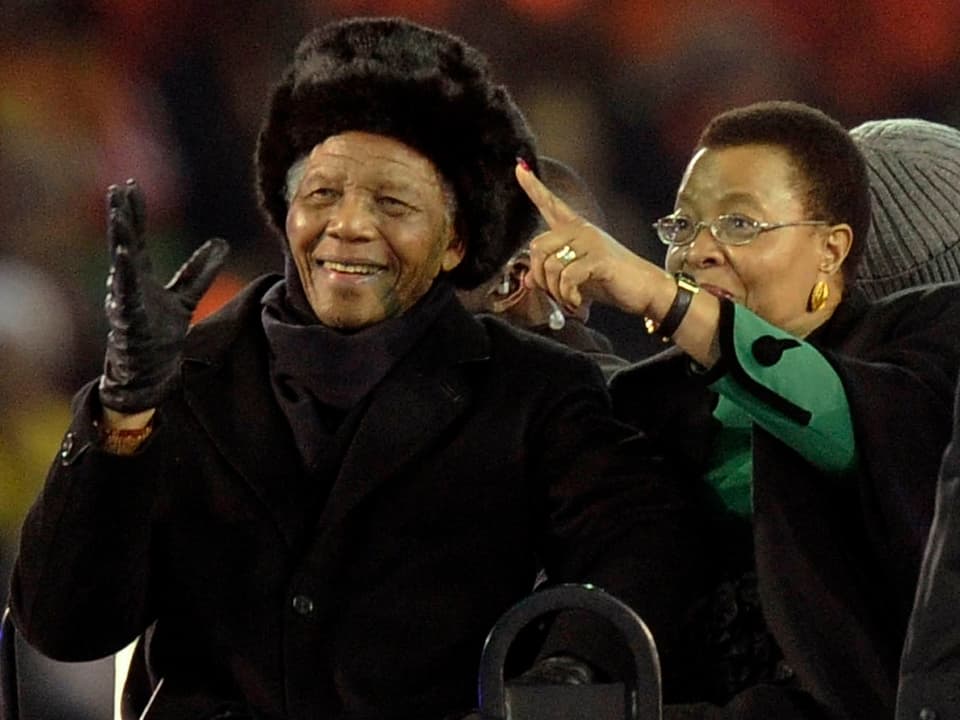 Mandela winkt, seine Frau neben ihm zeigt auf etwas in der Ferne