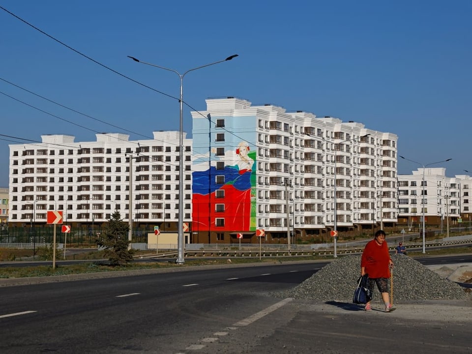 Eine Frau geht in der Nähe der neu gebauten Wohnblocks spazieren. Russische Flagge auf weissem Gebäude.