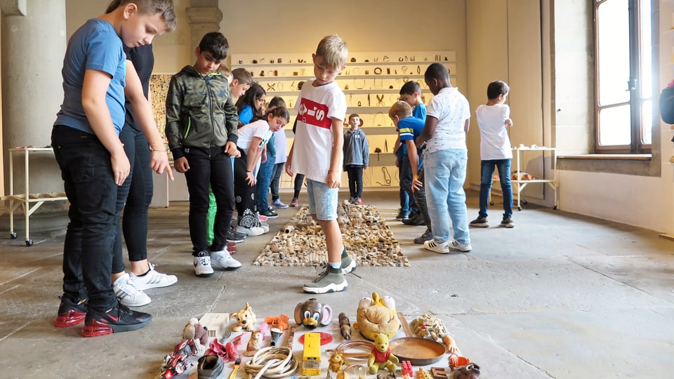 Kunstinstallation aus Abfällen, die am Boden liegen. Kinder betrachten intensiv die gesammelten Dinge.