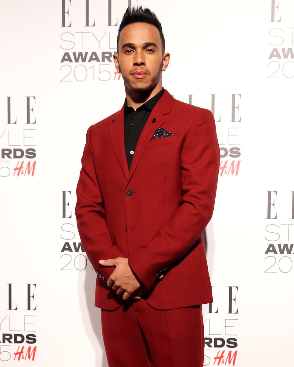Mann steht in rotem Anzug und schwarzem Hemd vor einer Fotowand.