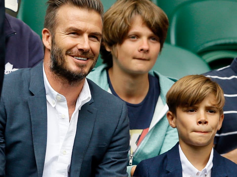 David Beckham sitzt neben Sohn Romeo. Beide mit blauem Jacket und weissem Hemd.