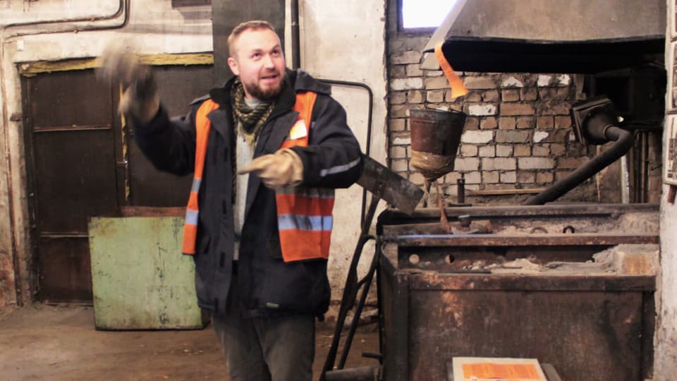 Ein Mann in orangem Gilet zeigt in einen Fabrikraum.