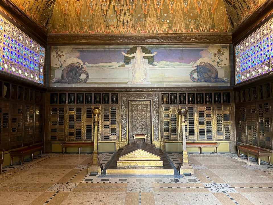 Innnenansicht eines mit Gold und Marmor dekorierten Krematoriums. In der Mitte ein Grab, zu den Seiten bunte Fenster