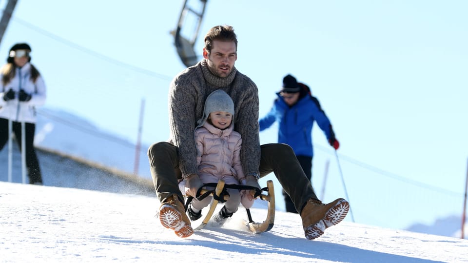 Tomaso Trussardi fährt mit seiner Tochter auf einem Holzschlitten den Berg herunter. 