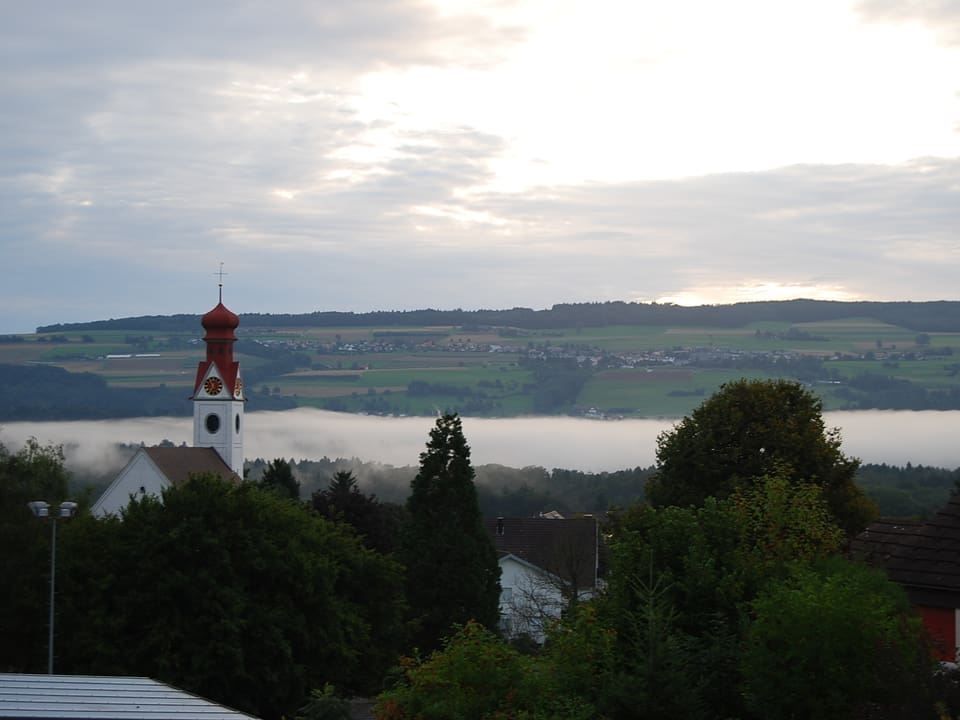 Eine graue Nebelschlange erstreckt sich entlang der Reuss. Im Vordergrund die Kirche von Niederwil im Kanton Aargau.