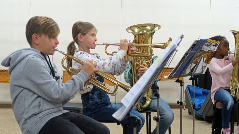 Drei Kinder spielen während des Musikunterrichtes auf Blasinstrumenten. 