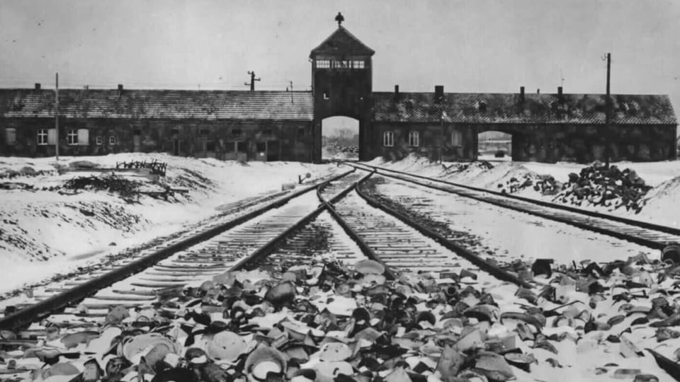 Historisches Bild des KZ Ausschwitz. Man sieht Zugschienen, die zum KZ führen und das KZ, aber keine Menschen. 