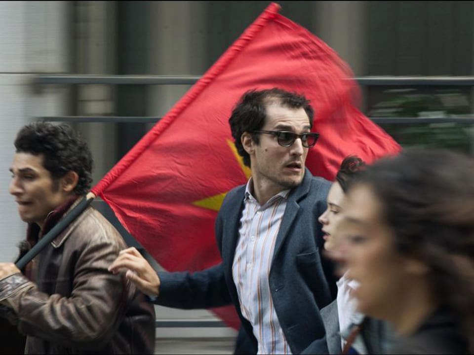 Filmstill: Junge Menschen rennen durch die Strasse, einer trägt eine rote Flagge.