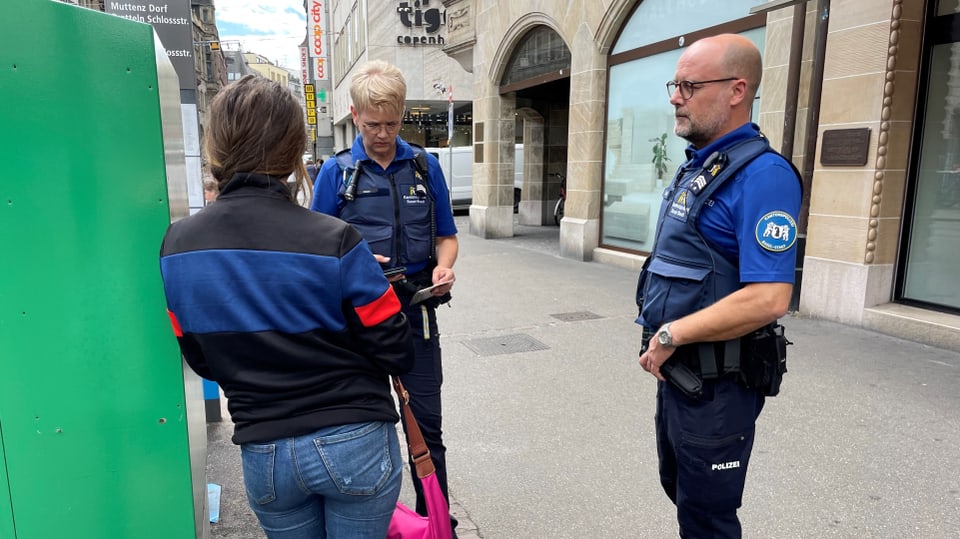 Eine junge Bettlerin wird von zwei Mitarbeitern der Basler Polizei kontrolliert. 
