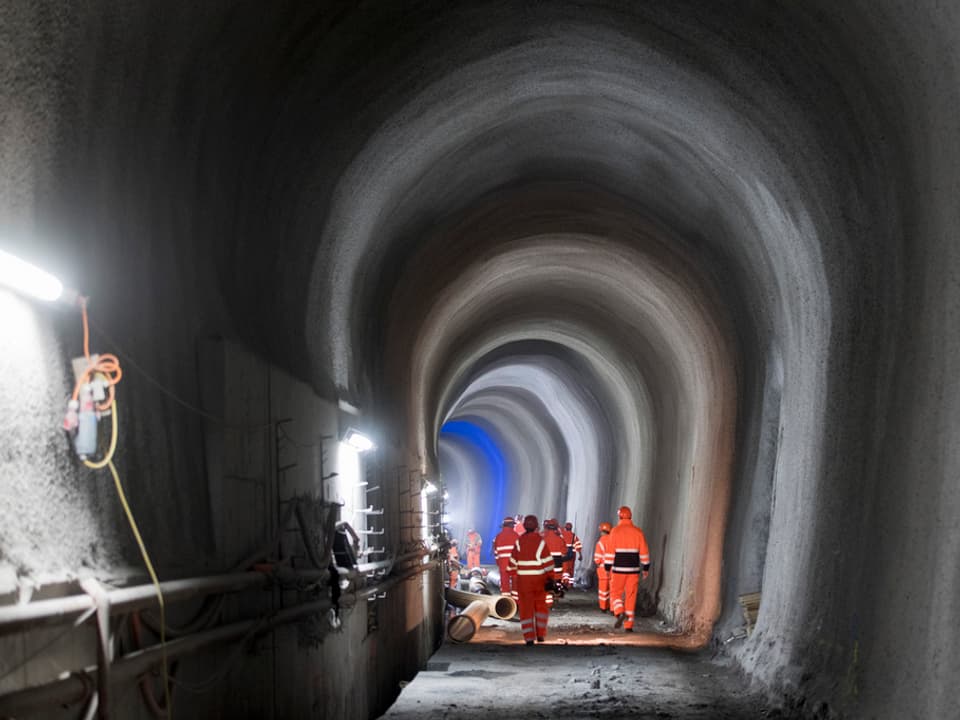 Bauarbeiter in orangenen Arbeitsgewändern in einer Tunnelbaustelle. 