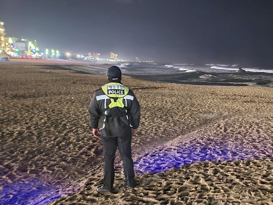 Ein Polizist steht an der Küste und schaut dem Wellengang entgegen.