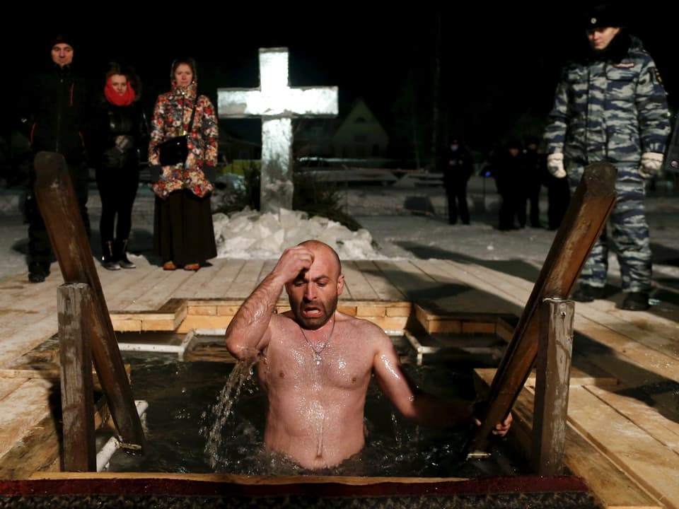 Ein Mann bekreuzigt sich im Eiswaser vor einem Kreuz aus Holz. (reuters)