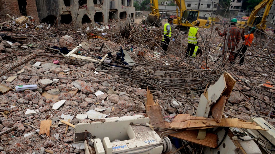Helfer stehen auf den Trümmern des eingestürzten Gebäudes in Bangladesch.