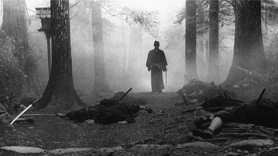 Ein Mann mit Schwert in einem Wald. Vor ihm liegen mehrere Personen am Boden