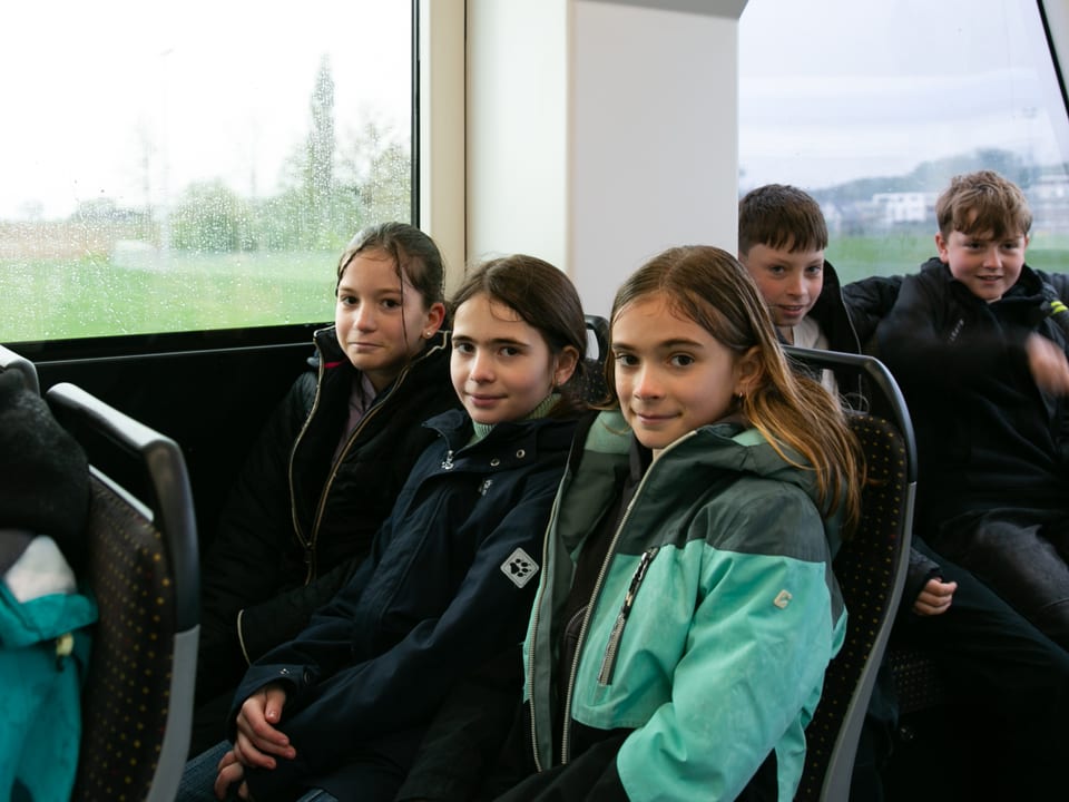 Drei Mädchen teilen sich zwei Sitze im Tram und schauen in die Kamera.