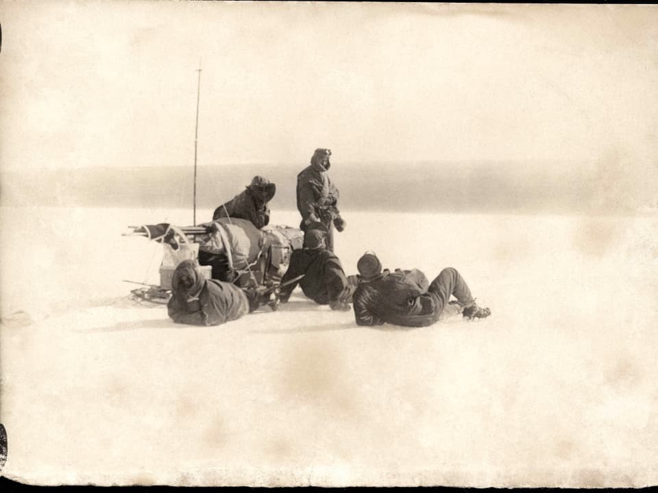Vier Männer machen neben dem Schlitten eine Pause im Eis der Antarktis.