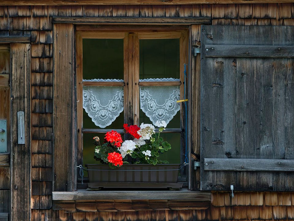 Holzhaus mit einem Geraniumkistchen vor dem Fenster.