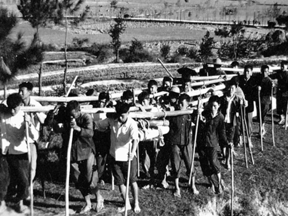 Landwirtschaftsarbeiter tragen Bambusstangen in den 1960er-Jahren. 