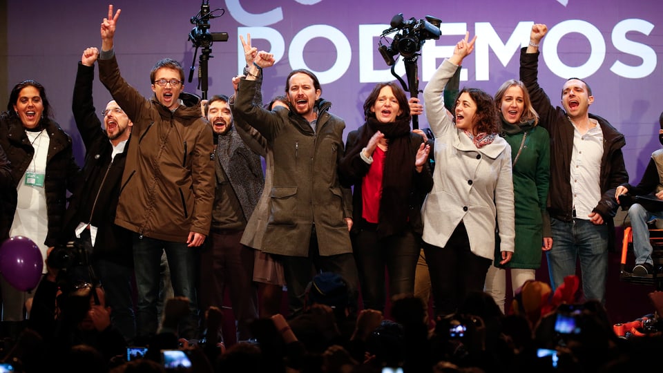 Podemos-Politiker jubeln auf einer Bühne.