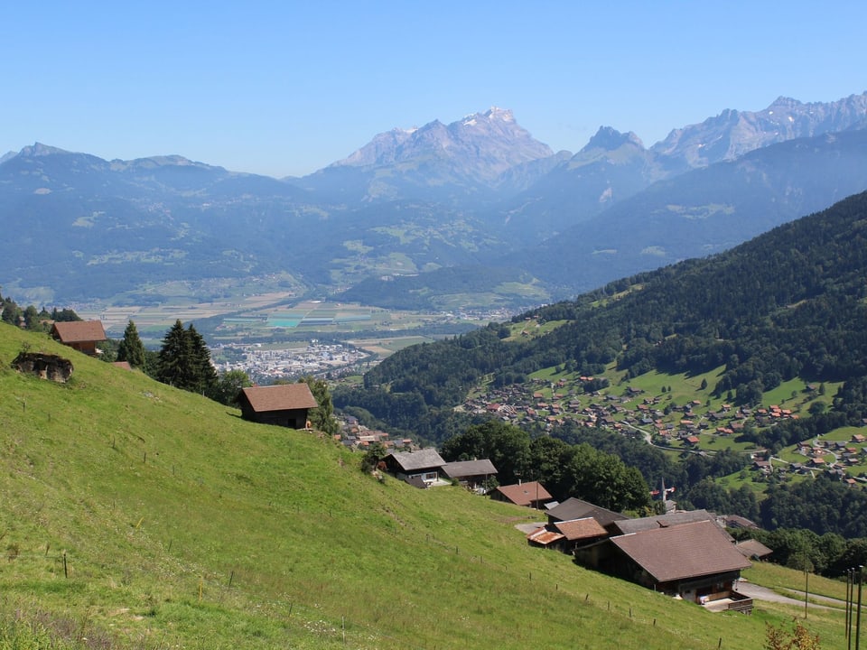 Bauernhäuser an einem steilen Hang, im Hintergrund ein Tal und Berge.