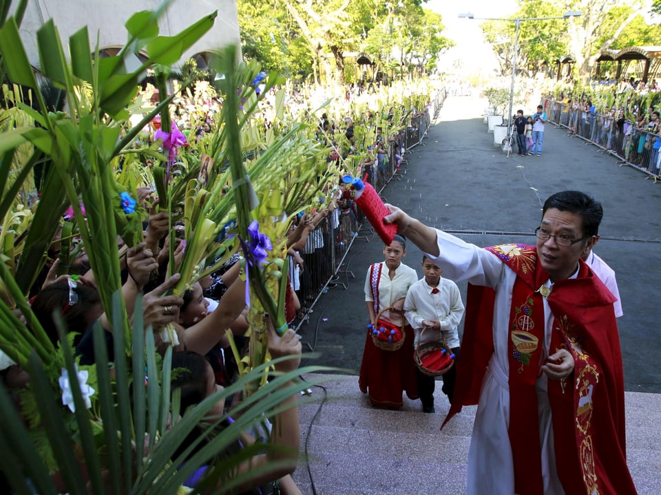 Philippinischer Priester segnet Palmen mit Weihwasser