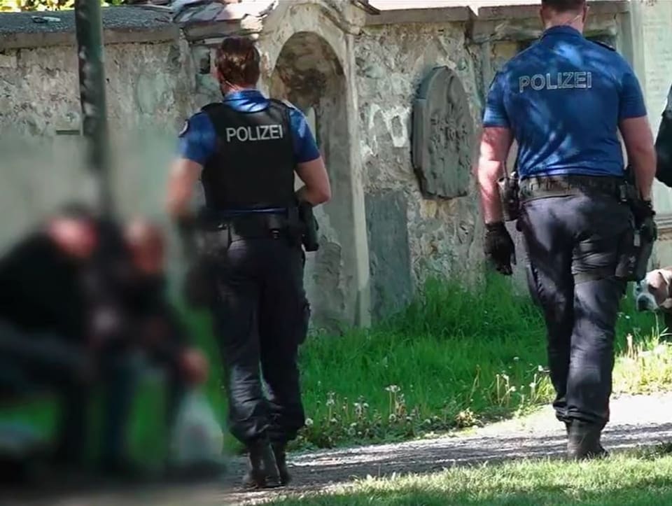 Zwei Polizisten gehen im Churer Stadtgarten zwei Männern auf einem Bänkli vorbei.