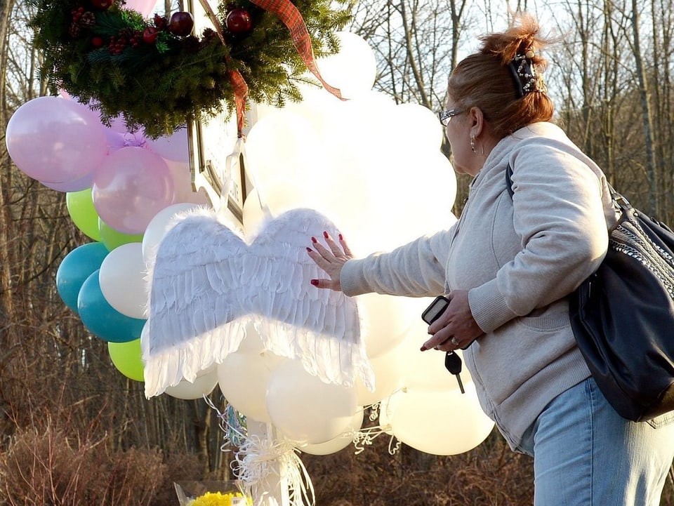 Eine Frau berührt ein paar Engelsflügel, dahinter schweben weisse Luftballons.
