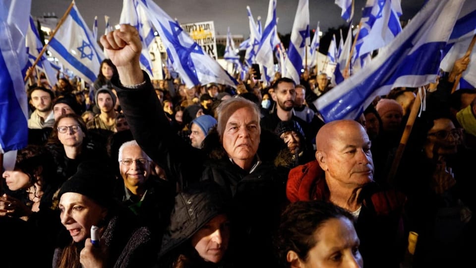 Demonstrierende versammelten sich in Tel Aviv. Einige halten eine Israel-Fahne. Ein Mann streckt die Faust in die Luft.
