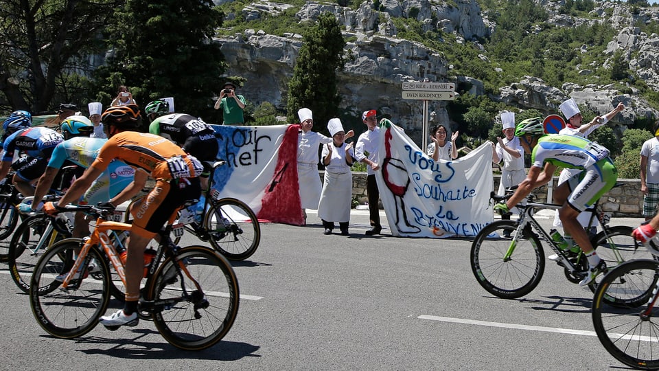 Fans in chefs attire encourage the pack of riders which cycles on its way during the 176.5 km fifth stage of the centenary Tour de France cycling race from Aix-En-Provence to Montpellier 