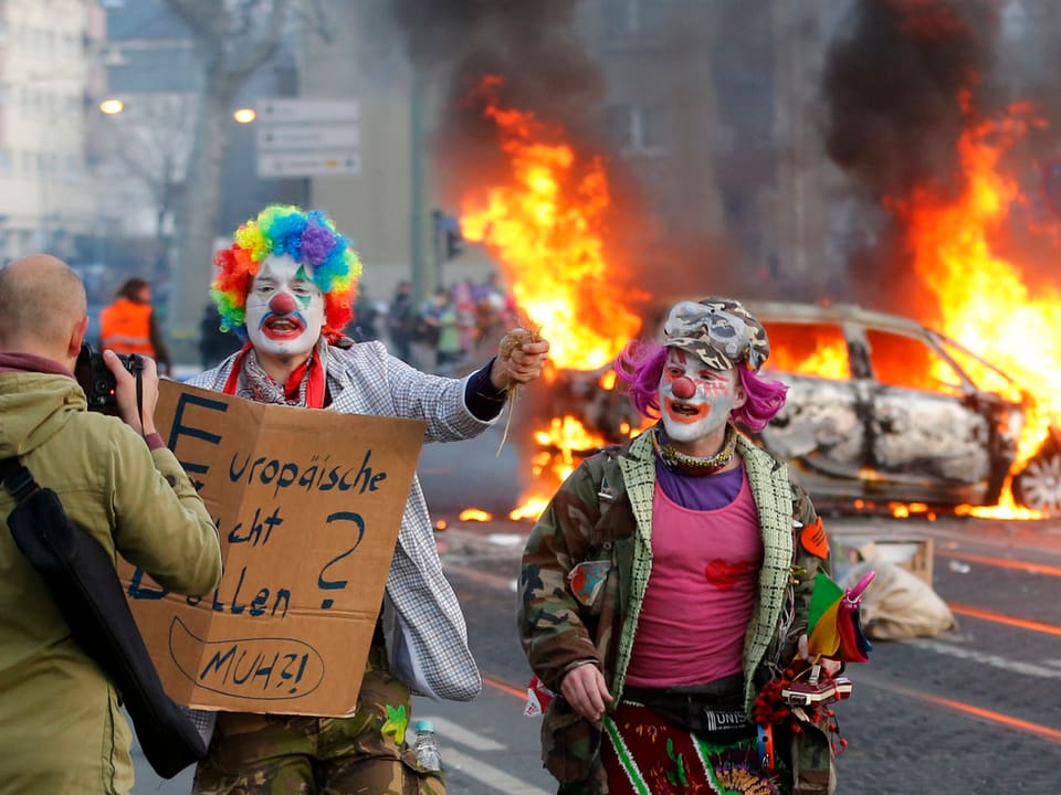 Als Clowns verkleidete Demonstranten vor brennenden Autos. (keystone)