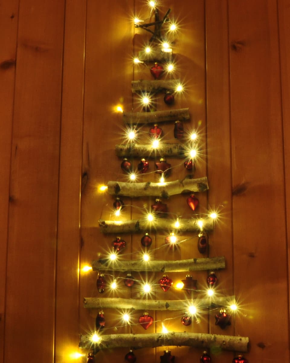 Verschieden lange Äste, die nach oben hin immer kürzer werden, so dass sie die Form eines Tannenbaums haben. Dazwischen Weihnachtskugeln und Lichterketten.
