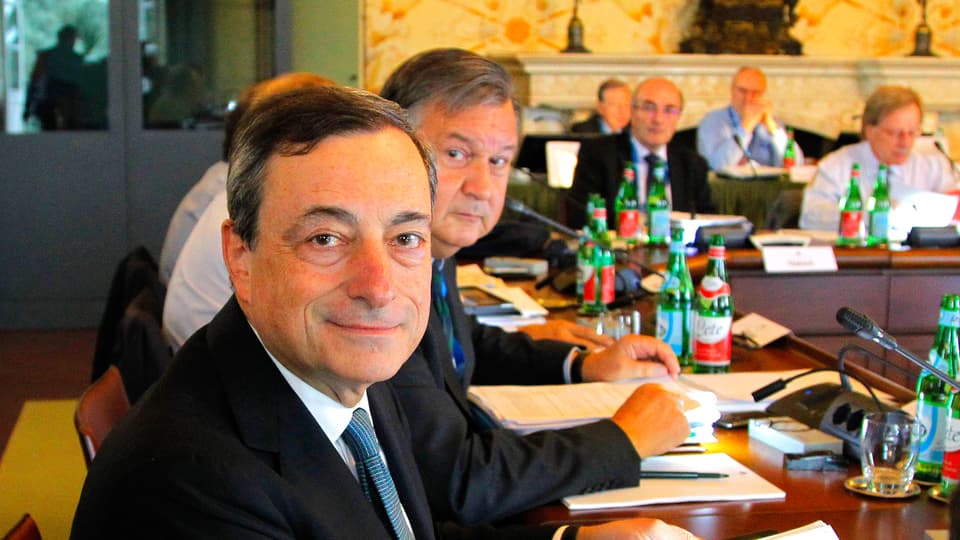EZB-Präsident Mario Draghi lächelnd an einem Konferenztisch.