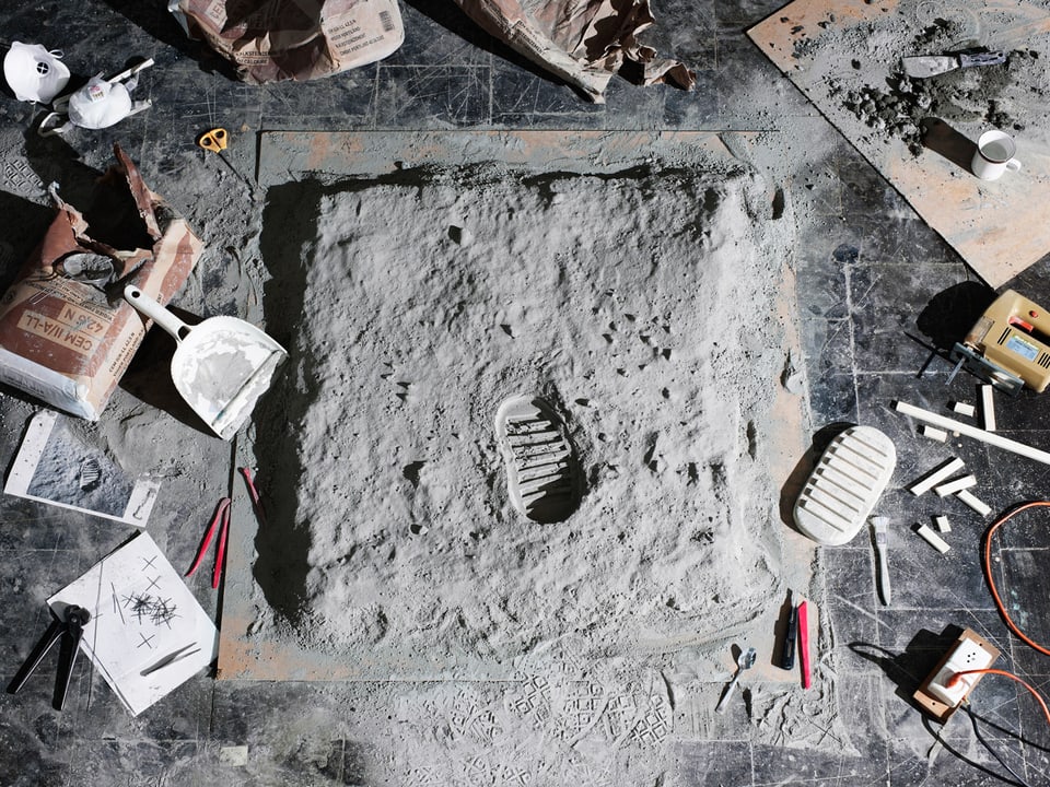 Ein Modell eines Fussabrdrucks in Mondsand mit Werkzeug drum herum.