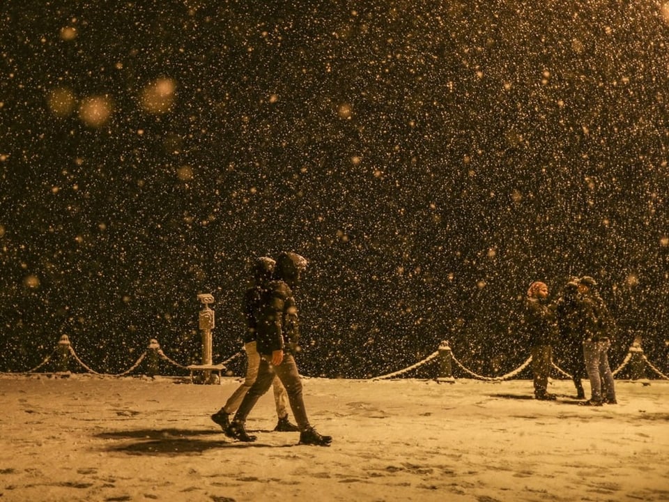 Dichter Schneefall im Dunkeln, Menschen laufen vorbei.