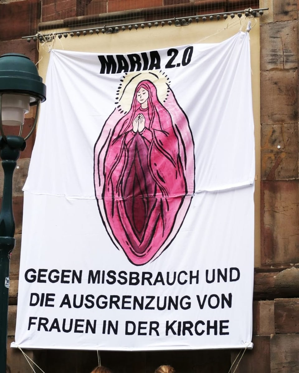 Ein Foto des Plakates an der Unikirche in Freiburg: Maria mit Heiligenschein und fleischfarbenen Kleid.
