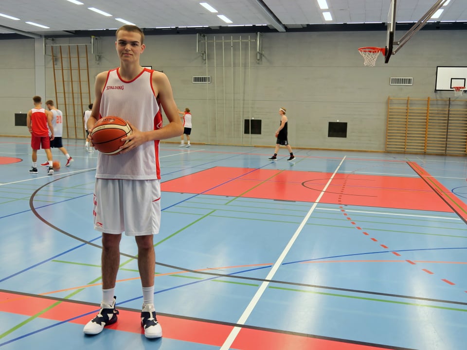 Basketballspieler steht mit Ball in der Hand in der Halle.