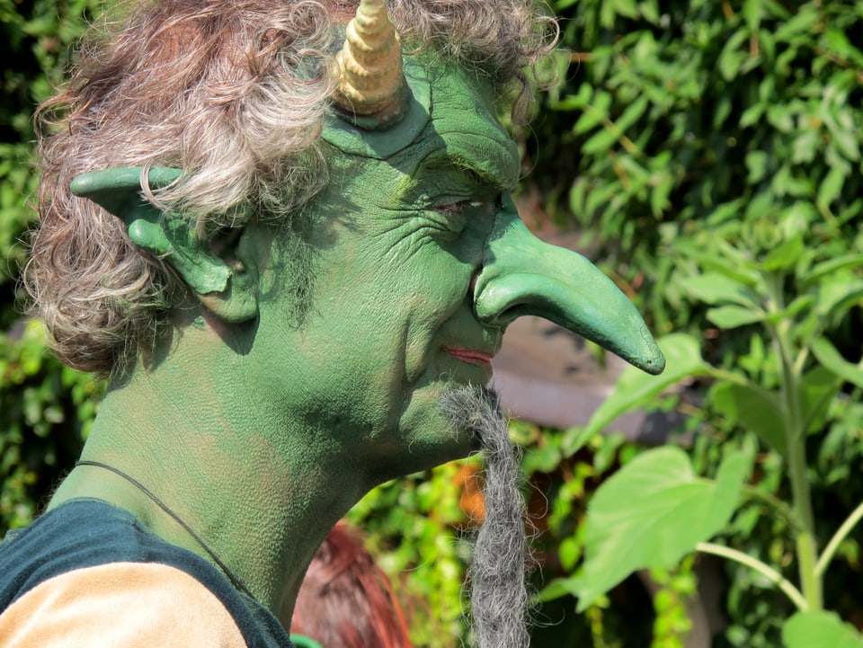 Mann, grün geschminkt, mit langer Nase, spitzen Ohren und Hörnern