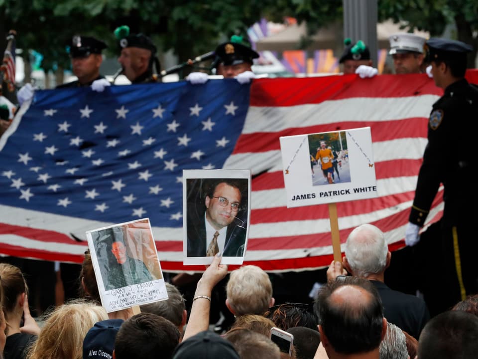 Polizisten tragen eine grosse USA-Flagge. Angehörige der 09/11-Opfer halten Fotos ihrer Liebsten hoch. 