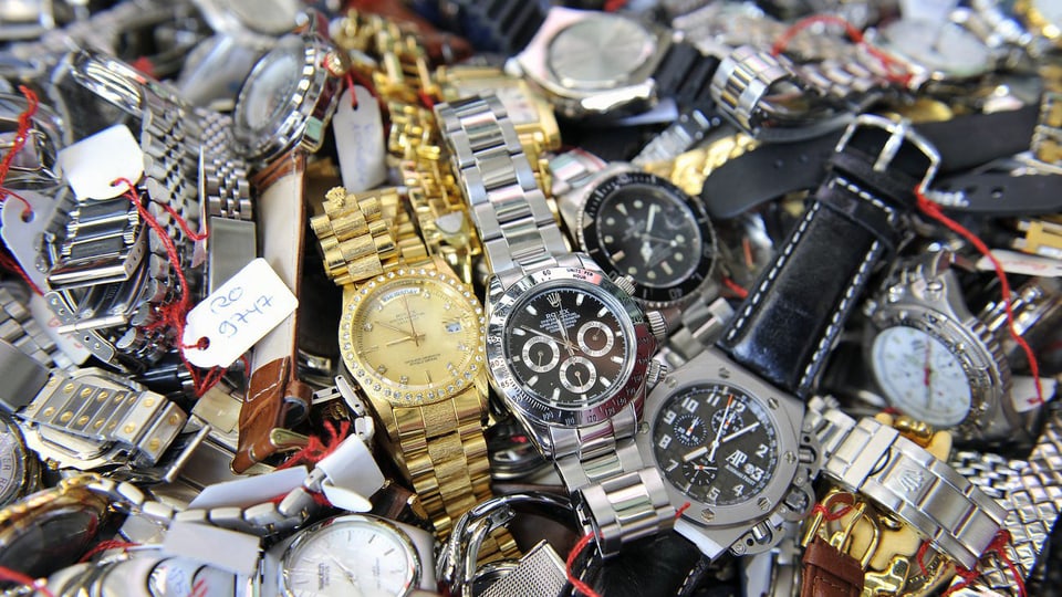 Viele sichergestellte, gefäschte Uhren auf einem Haufen.