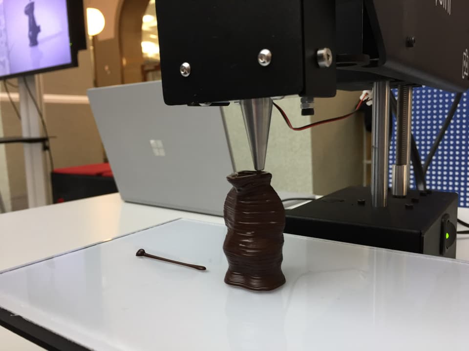 Ein Drucker formt aus Schokolade eine Globifigur. 