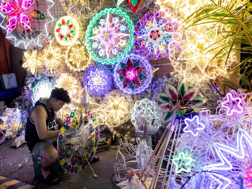 Ein Mann arbeitet inmitten der leuchtenden, blumenförmigen Weihnachtslaternen.