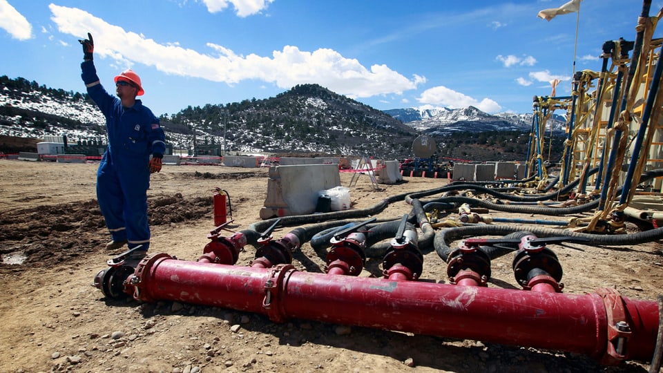 Ein Mann steht neben grossen roten Leitungen, die zu einer Gas- und Ölförderanlage gehören.