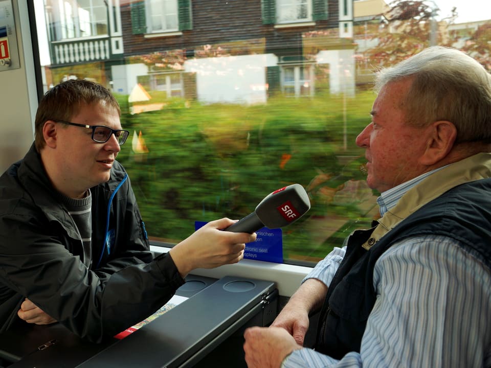 Im Zugsabteil interviewt ein Radioreporter einen ehemaligen Lokomotivführer.
