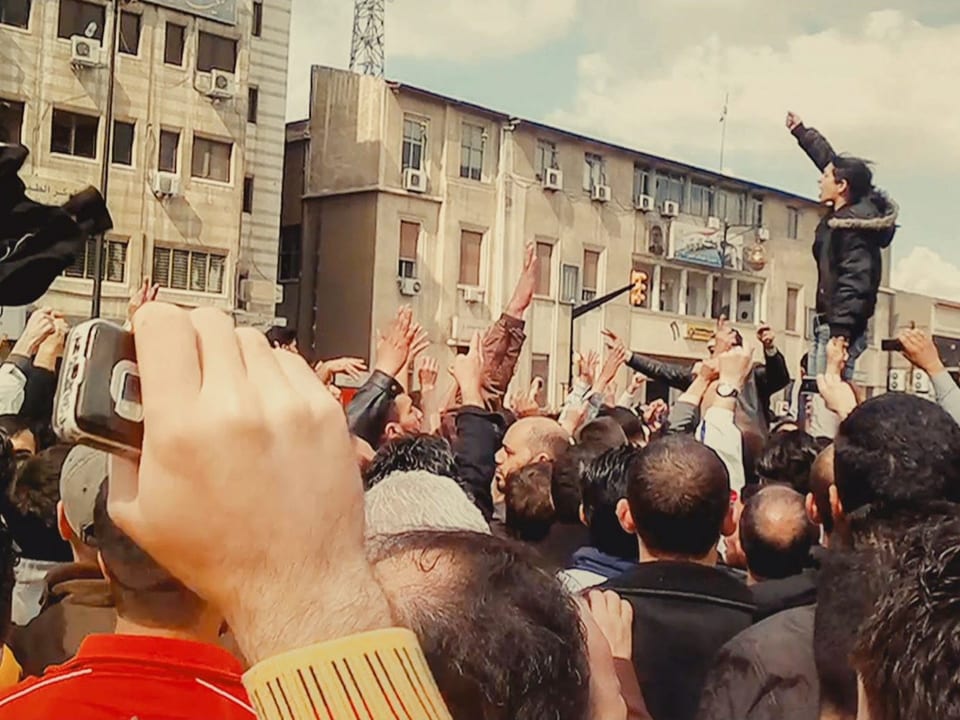 Filmszene: Menschenmenge, mehrere Person strecken die Arme in die Luft