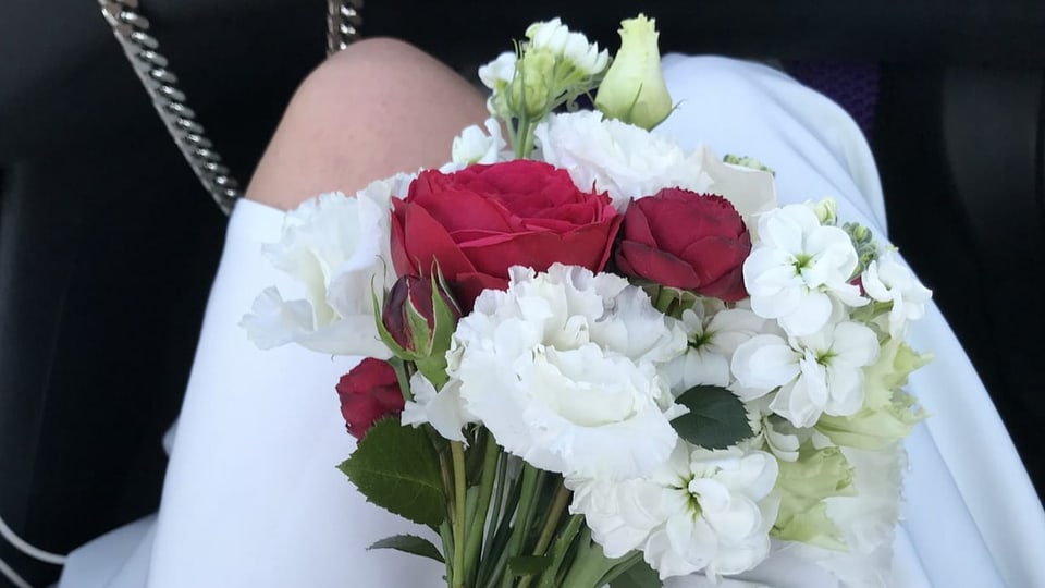 Die Beine einer Frau aus der Vogelperspektive in einem Hochzeitskleid und weiss-roten Blumen