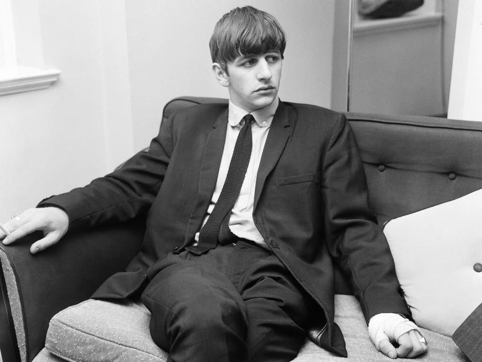Portrait des jungen Ringo Starr. Schwarz-weiss-Aufnahme, wie er auf einem Sofa sitzt. Er trägt einen Anzug.