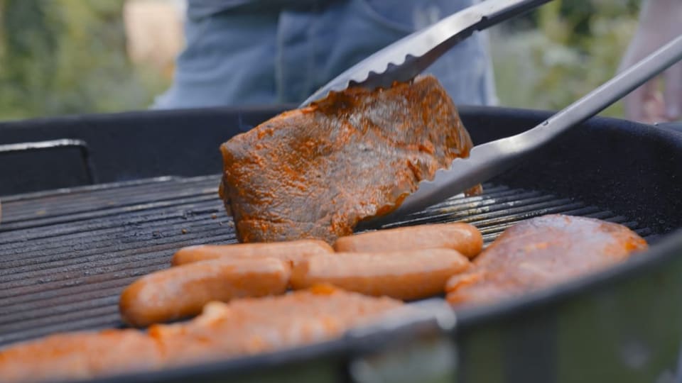 Ein Stück Fleisch wird mit einer Grillzange gewendet.